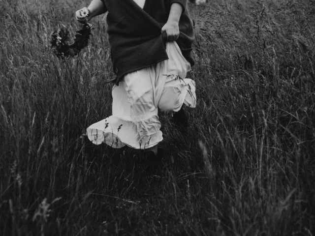 grayscale close up photo of woman holding flower crown running in grass field